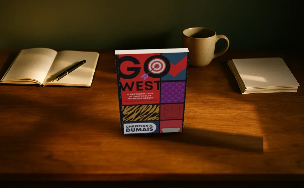 Go West standing on a wooden writer's desk with a notebook and a mug, at 970 by 600